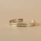 Brazalete rígido abierto de plata con apliques de oro y tres circonias engarzadas.