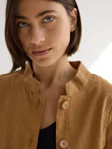 Chaqueta color marrón claro de lino y algodón, con cuello mao, cierre frontal con botones de madera y bolsillos laterales.