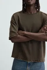 Camiseta marrón de corte holgado, cuello redondo y manga corta. Tiene un efecto lavado y terminaciones irregulares.