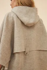 Capa amplia color beige con capucha, cierre metálico y bolsillos delanteros. Espalda con canesú y botones laterales para generar la manga. Confeccionada en lana fina sin teñir.