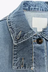 Chaqueta de denim celeste con cuello alto, manga larga con trabilla y bolsillos laterales. Presenta detalle de pliegues en la espalda y cierre frontal con botones ocultos.