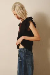 Remera negra sin mangas con volados en los hombros y escote en V. Incluye un collar largo de cuentas con un nudo decorativo. Jeans de tiro bajo.