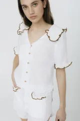Blusa blanca de lino con cuello y mangas cortas con volados con borde de crochet marrón.