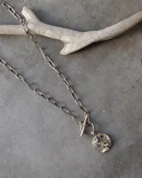 Collar plateado con cadena de eslabones y dije circular texturizado.