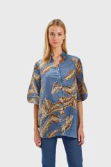 Camisa celeste con estampado de hojas marrones, de mangas 3/4 abullonadas y cuello clásico.