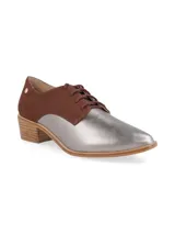 Zapato acordonado de cuero color plateado con puntera fina y detalle de cuero marrón en el talón.