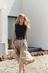 Vestido midi con cuerpo negro sin mangas y falda plisada color beige. Incluye cinturón negro con hebilla rectangular.