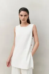 Blusa sin mangas negra de punto suave y fluido, con silueta larga y recta. Presenta botones dorados en los laterales.