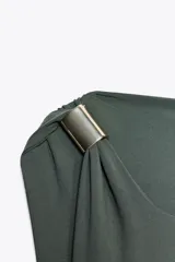 Vestido midi negro de punto, con cuello asimétrico, manga sisa, aplique metálico dorado en el hombro y drapeado lateral.