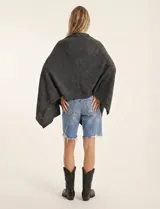 Poncho tejido de punto grueso, color mostaza/mostaza oscuro, con cuello redondo y caída amplia.