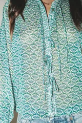 Camisa de manga larga con estampado floral en tonos verde y azul. Tiene cuello solapa, cierre frontal con botones y lazadas en los puños.