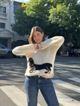 Sweater tejido color crema con cuello y puños acanalados en color naranja. Presenta un diseño bordado de un perro salchicha negro con un moño naranja.