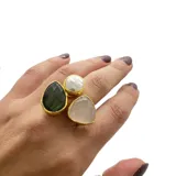 Anillo artesanal con engarce dorado, con tres piedras irregulares: una perla barroca, un cuarzo rosa facetado y una piedra de la luna. El tamaño es regulable.