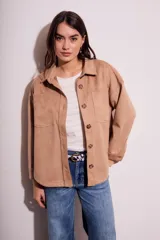 Sobrecamisa color beige de gamuza sintética con cuello camisero, cierre frontal con botones a tono, dos bolsillos de parche en el pecho, corte oversize y mangas largas con puños abotonados.