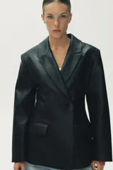 Blazer entallada negra de efecto piel, con cuello solapa y manga larga. Tiene bolsillos de plastrón en el delantero, costuras marcadas y forro interior combinado a tono. El cierre es frontal con botón interior y exterior.