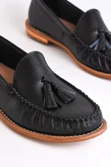 Mocasines negros de cuero con borlas y costuras decorativas.