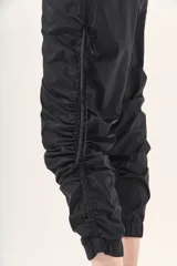 Pantalón jogger negro de nylon con elástico ancho en la cintura, puños elásticos ajustables y lazos laterales para fruncir.