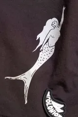 Short de baño negro con cintura elástica y cordón ajustable. Presenta bordados de sirenas en ambas piernas, bolsillos laterales y trasero con cierre. Incluye suspensor de malla fina hipoalergénico.