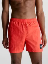 Short de baño rojo coral de largo medio, con cintura elástica y cordón ajustable. Incluye bolsillos laterales y trasero, forro de malla y logo de Calvin Klein en el lateral.