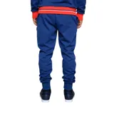 Pantalón de jogging azul con puños ajustados y cordón en la cintura. Presenta el escudo del Club Nacional de Football en la pierna izquierda y un logo estilizado en la pierna derecha.
