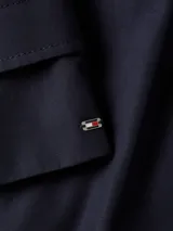 Gabardina corta azul marino de Tommy Hilfiger, con botonadura simple, cuello inglés, trabillas en los hombros, solapa de protección delantera y trasera, puños con tira y botón, y logo metálico en el puño.