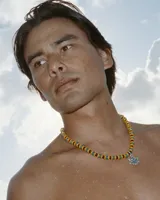 Collar de cuentas de colores verde, amarillo y negro, con dije de hoja de marihuana plateada.