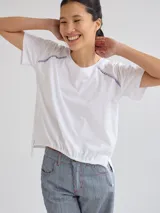 Remera blanca de algodón suave con detalle de bordado en los hombros y cordón ajustable en el ruedo.
