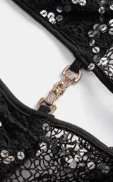 Conjunto de dos piezas negro, compuesto por un top halter con abertura frontal y detalle de hebilla dorada, y una falda larga transparente con lentejuelas plateadas dispuestas en líneas diagonales y flecos colgantes.
