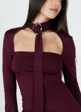 Vestido corto color borgoña, ajustado al cuerpo, con escote recto, mangas largas acampanadas y gargantilla con hebilla plateada.