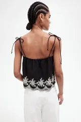 Top negro de algodón con breteles finos que se atan en moño y detalle de bordado floral blanco en el ruedo.