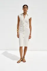 Vestido midi color gris topo, de cuello camisero y escote pico con manga corta. Tiene detalle de drapeado lateral y cierre frontal con botones metálicos.