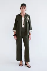 Camisa verde militar de manga larga con puños color crema, cuello clásico y cierre frontal con botones. Tiene un bolsillo en el pecho con bordado de una palmera color crema.