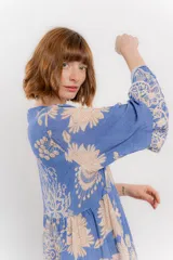 Vestido largo azul con estampado floral en tonos beige, confeccionado en viscosa. Presenta escote en V, botonadura completa en el frente y mangas largas con volados.