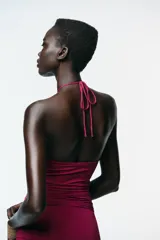 Vestido color fucsia de poliamida con cuello halter con lazada y detalle de aplicación metálica en forma de sol.