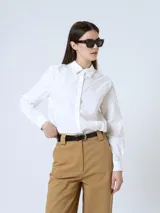 Camisa blanca de corte recto, con cuello clásico, cierre frontal con botones y mangas largas con puños abotonados.