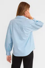Camisa celeste de algodón con cuello camisero, mangas largas abullonadas con bordados y cierre frontal con botones.