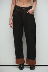 Pantalón de jean negro, corte recto y tiro medio/alto, con bolsillos clásicos y botamanga rebatida con interior color marrón.