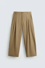 Pantalón color beige de corte ancho, con pliegues frontales dobles, bolsillos laterales y traseros de vivo. Largo cropped y cierre frontal con cremallera y botón.