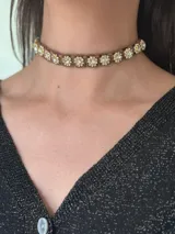Gargantilla tipo choker con tiento trenzado color marrón y apliques de flores con brillantes. Se cierra con cadena de acero quirúrgico y gancho para ajustar.