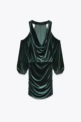 Vestido corto de terciopelo verde esmeralda, con escote fluido, mangas largas abullonadas y aberturas en los hombros.