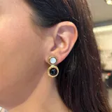 Caravanas artesanales de bronce con dos piedras naturales engarzadas en disposición vertical, una de color azul y otra gris. Presentan un acabado rústico con detalles circulares y cierre de presión.