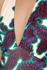 Traje de baño entero con estampado floral en tonos morado y verde sobre fondo blanco. Diseño con escote en V pronunciado y tirantes que se atan al cuello.