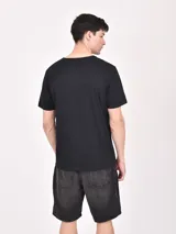 Remera negra de mangas cortas con estampado de palmeras y texto en color naranja.