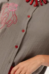 Camisa verde de silueta oversize con cuello camisero y manga 3/4. Tiene bordados de coral y caracol en el frente y botones a tono.