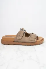 Sandalias bajas color visón, con dos tiras anchas de cuero con hebillas metálicas ajustables y suela marrón con diseño antideslizante.