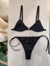 Conjunto de bikini negro con textura acanalada. El corpiño es de corte triangular con breteles regulables y detalle de aro metálico en el centro. La bombacha es tipo colaless con tiras finas regulables en los laterales.