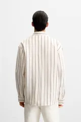 Camisa de hombre regular fit, color blanco con rayas verticales negras, cuello solapa, manga larga con puños abotonados y cierre frontal con botones.