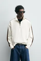 Sudadera color crudo de corte relaxed fit, con cuello alto con cremallera y mangas largas con banda marrón a contraste.
