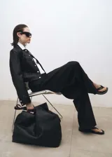 Chaqueta corta de cuero negro con cuello camisero, cierre frontal con botones a presión plateados, bolsillos laterales y puños abotonados.