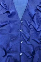 Camisa azul con escote en pico, cierre frontal con botones, mangas largas abullonadas con elástico en los puños y detalle de volantes en el frente.